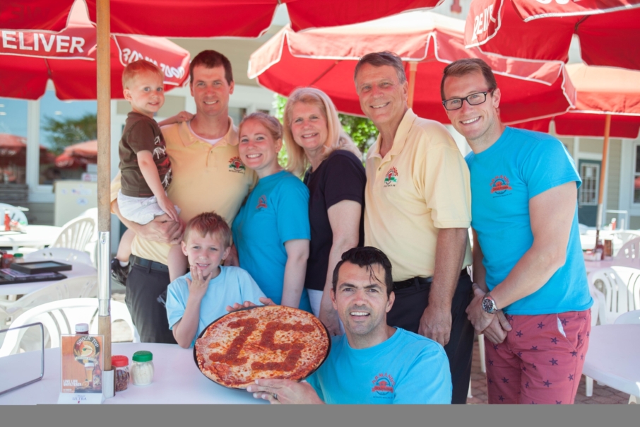 Operation SEAs the Day supporter Armand’s Pizzeria celebrates 15 years Date Published: June 24, 2016 By Tripp Colonell Staff Reporter Coastal Point • Tyler Valliant: The Drosdzal family is celebrating 15 years of serving the Bethany Beach area at Armand's Pizzeria & Grille. Coastal Point • Tyler Valliant: The Drosdzal family is celebrating 15 years of serving the Bethany Beach area at Armand's Pizzeria & Grille. The Drosdzal family at Armand’s Pizzeria & Grille is in the service industry. That much is obvious. Celebrating a major anniversary this summer, they’ve been in the service industry now for going on 15 years. Much of that service has been in the form of delivering the goods — specialty pizzas in their signature deep-dish style, signature pastas, such as Riley’s homemade ravioli stuffed with Valentino’s ricotta cheese, or an array of fresh salads, subs, seafood entrees and other traditional Italian fare. But not-so-obviously, the Drosdzals have also been doing their best to deliver on serving those who serve the country as well. “We’ve been blessed here, and we wanted to give back, to all of the community,” said Ron Drosdzal, owner, operator and family patriarch. It was 2013 when Operation SEAs the Day — an organization dedicated to helping wounded veterans their families — launched Warrior Beach Week in Bethany Beach. That was the same year that things became about much more than pizza and pasta for Drosdzal, and his family, too. “The bottom line is, when Operation SEAs the Day — when that foundation started — it changed Bethany, and it changed me. I got a whole different perspective on all the issues,” Drosdzal said. “I’ve become friends with so many of [the veterans]. We want to make their day.” “It’s heartfelt, because none of us were in the military — it’s all about them,” said Drosdzal’s son, Brian Drosdzal, a server at Armand’s, of the family’s way of giving back to their country. “What’s amazing is it’s not just us — the whole community really comes together. “We’ll get customers that didn’t know that we were supporting the cause, and if they overhear us comping the meals, they’ll try to give us money to cover our food cost.” Obviously, those customers’ generosity is appreciated, but the money is not accepted because, for the Drosdzals, giving back has become not only selfless, but contagious. Not only does the restaurant support causes including SEAs the Day, but also whatever they can in the community, wherever they can do it. There are catering functions for the Bethany Beach and Millville volunteer fire companies; laying out an Italian-inspired spread for the annual Sea Colony lifeguard competition, Sea Colony Sharks’ swim team and Bethany Beach First Responders Triathlon; supporting organizations such as St. Ann’s church and Make-A-Wish, or even just events at Lord Baltimore Elementary, where Drosdzal’s grandson, Riley (of Riley’s Ravioli fame), goes to school with his brother Zack (the collective philanthropic future of the business). While working full-time as a federal consultant, running the family busienss, supporting the community and still trying to find time for a round of golf or a beach day every once in a while hasn’t been easy for Ron Droszdal — or any of the Droszdals, for that matter — they said that, unquestionably, it has been worth it. Of course, Ron Droszdal has certainly had some help in making it all work, with every aspect of Armand’s being a family affair — just like it has been now for 15 years. Droszdal’s older son, Matt Droszdal, works as a manager and heads up the shop’s beach delivery service. Brian, and son-in-law Carlos Mandacaru, serve tables, while daughter,Kathleen Droszdal runs the counter on the weekend when not working her full-time job in Silver Spring, Md. His wife, Karen Droszdal, helps out wherever she can, too — coming in especially handy when 30,000 brand-new menus need to be delivered from over the Bay Bridge. And his nephew, Justin Venasco — a gourmet chef — heads up anything and everything concerning the kitchen, including coming up with the recipes for all the sauces and pastas, from scratch. Not only does his family share his commitment to serving food but to serving the community as well. “It made me cry,” said Manducara of his first experience with SEAs the Day. “To see how happy they were in life, and the struggle they had. It made me realize how we complain so much for nothing. And then to see what they have and the struggle they go through, and they don’t complain, they just say ‘Thank you.’ It just made me cry.” “I follow his footsteps,” said Matt Droszdal of his father. “He’s been my role model since I started doing it at 19 years old. I started out as a carry-out guy and then I climbed the ladder, basically. I have two of my own kids involved now.” When they’re not making pies for Warrior Beach Week or lifeguard competitions, the crew at Armand’s is just making pies. House favorite pizzas include the Original Chicago Combo, with pepperoni, sausage, fresh mushrooms, green peppers and white onions; the Carlos Garden Delight, with broccoli spinach, red onions, red bell peppers, minced garlic and cheddar cheese; and the Crabby Abby Pizza, with lump crab meat, artichoke hearts, minced garlic and sun-dried tomatoes, topped with Old Bay seasoning and served with a garlic butter sauce. Other out-there specialty pies include the “Hawaii Pie O,” Bacon Cheeseburger, Pesto Chicken, and the “Armand’s Hammer” — which the crew joked that they could “barely get in the oven.” For non-Chicago-style enthusiasts, traditional-crust pizzas are also available, as well as favorites including a white pizza, triple cheese and Margherita. According to the Drosdzals, while the pizzas are a hit, the traditional Italian pastas are just as much so, and the restaurant also offers specialty subs, such as “Jack’s Famous Steak & Cheese,” burgers, appetizers including jumbo wings, bruschetta and “Tonilynn’s Mozzarella Sticks,” salads made from fresh local produce, desserts and a kid’s menu as well — all available to dine inside or out, for carry-out, or for delivery right to the beach. No matter what kind of service, however, Ron Drosfzal said that none of it would be possible without the support they’ve received from the community over the past 15 years. “We’re very fortunate,” he said. “It’s just gotten to the point where it really has grown past my expectations — it’s from all the local support.” Armand’s Pizzeria & Grille is located at 33548 Marketplace at Sea Colony (Route 1 and West Way). In the summer, the restaurant is open seven days a week for both lunch and dinner. They close down for a month in the winter (from Thanksgiving to Christmas), to be able to host veterans for Thanksgiving dinner and spend some family time, but open back up Thursday through Sunday in the off-season.